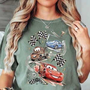 A person wearing a green t-shirt with a graphic design featuring animated cars from the Disney Pixar movie Cars.