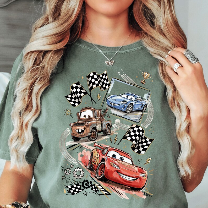 A person wearing a green t-shirt with a graphic design featuring animated cars from the Disney Pixar movie Cars.