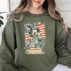 A woman wearing a green sweatshirt with a graphic of Mickey Mouse holding up the Statue of Liberty.