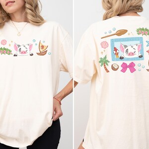 A woman wearing a white t-shirt with a cartoon pig design and various colorful illustrations on the back.