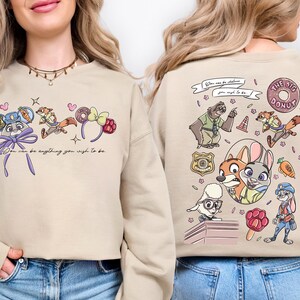 a woman wearing a beige sweatshirt with a colorful cartoon-style design on the front and back.
