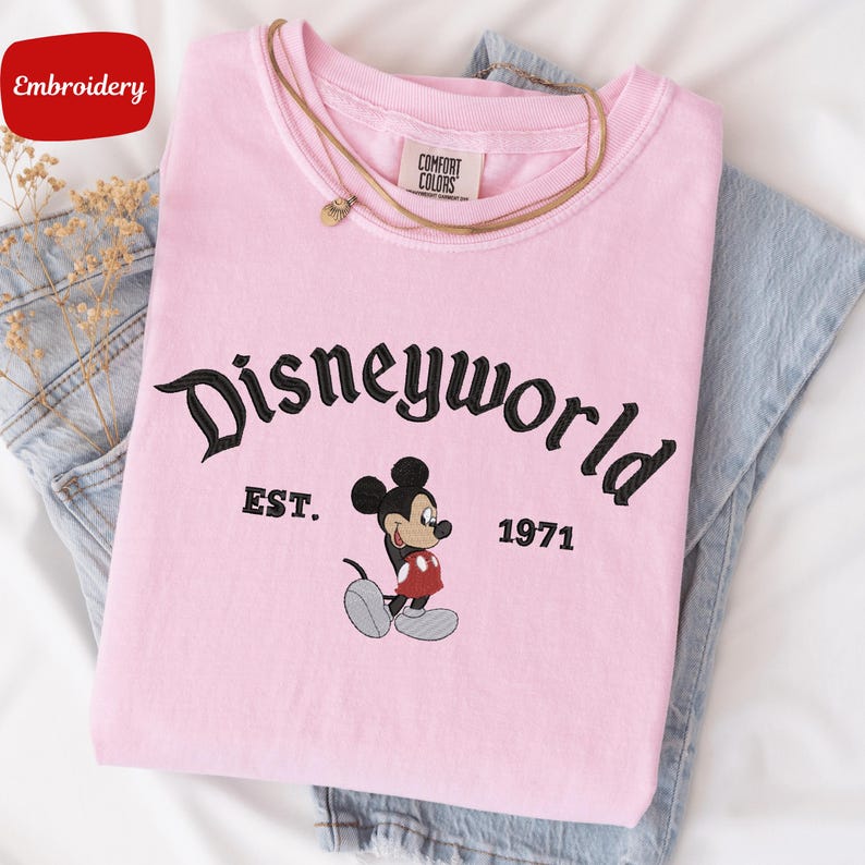 A pink t-shirt with the text "Disneyworld" and a Mickey Mouse graphic, along with the text "EST. 1971" printed on it.