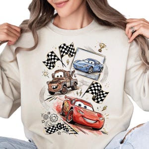A woman wearing a white sweatshirt with a graphic design featuring cartoon cars and checkered flags.