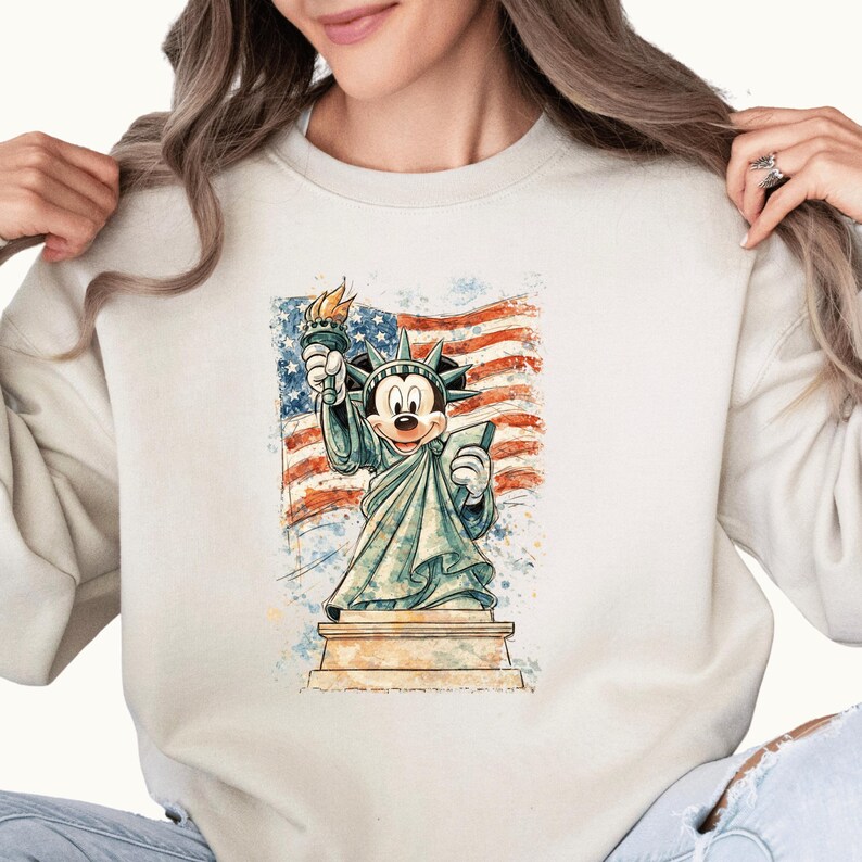 A woman wearing a white sweatshirt with a graphic of Mickey Mouse holding up the Statue of Liberty.