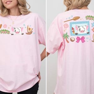 A woman wearing a pink t-shirt with a cartoon pig and various other cartoon-style objects and characters on it.
