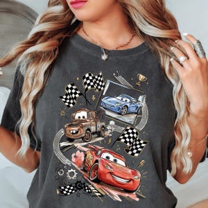 A woman wearing a gray t-shirt with a graphic design featuring cartoon cars and checkered flags.