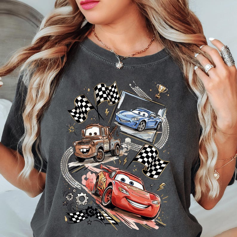 A woman wearing a gray t-shirt with a graphic design featuring cartoon cars and checkered flags.