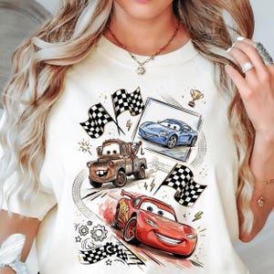 A white t-shirt with a graphic design featuring characters from the animated movie Cars, including a tow truck, a blue car, and a red car.