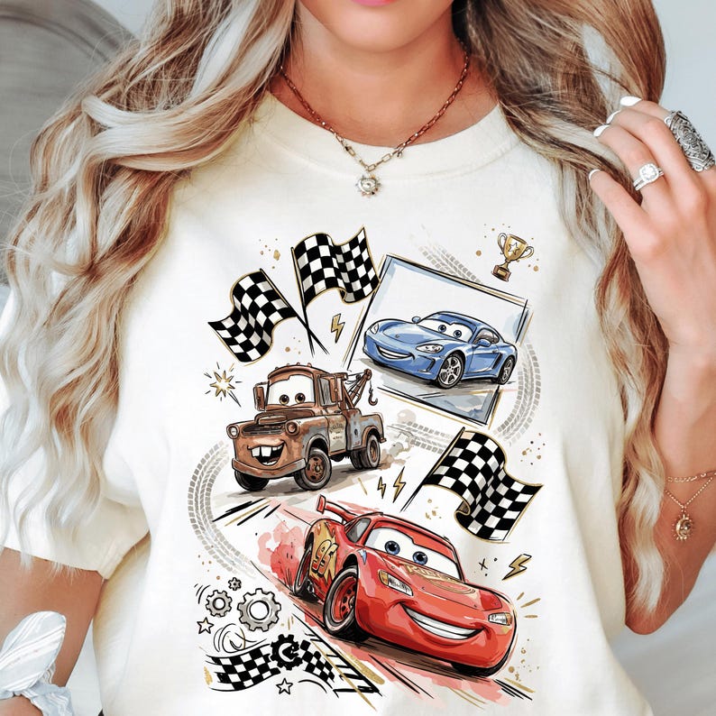 A white t-shirt with a graphic design featuring characters from the animated movie Cars, including a tow truck, a blue car, and a red car.