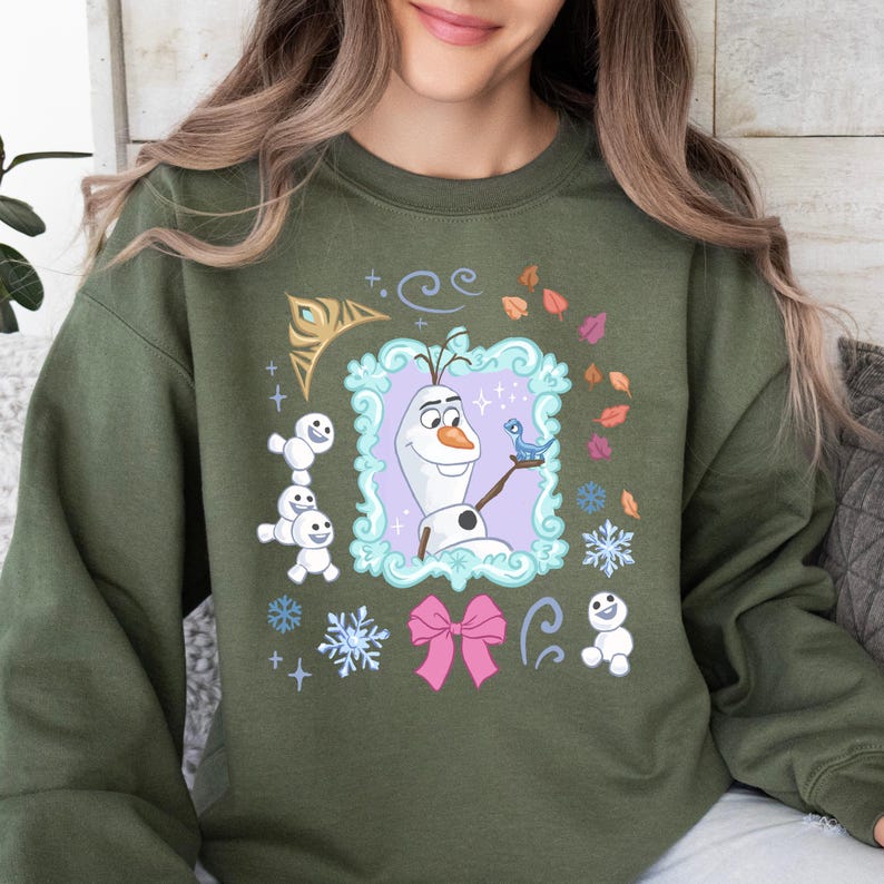 A woman wearing a green sweatshirt with a graphic design featuring characters from the Disney movie Frozen.