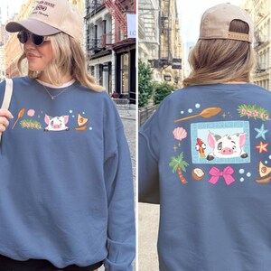 A woman wearing a blue sweatshirt with a cartoon pig design and various colorful illustrations on the back.
