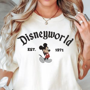A woman wearing a white t-shirt with the text "Disneyworld EST. 1971" and a Mickey Mouse graphic.