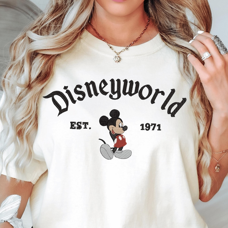 A woman wearing a white t-shirt with the text "Disneyworld EST. 1971" and a Mickey Mouse graphic.