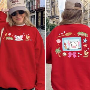 A woman wearing a red sweater with a pig design and various other decorative elements, including a palm tree, starfish, and other whimsical illustrations.