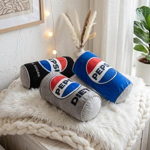 May include: Three cylindrical Pepsi-themed pillows in black, blue, and gray. Each pillow features the Pepsi logo in red, white, and blue. The gray pillow is labeled "Diet" and the black pillow is labeled "No Sugar".