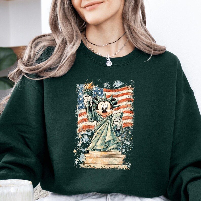A woman wearing a green sweatshirt with a graphic of a cartoon character, specifically Mickey Mouse, holding a torch and standing on a pedestal.