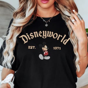 A woman wearing a black t-shirt with the text "Disneyworld EST. 1971" and a Mickey Mouse graphic.