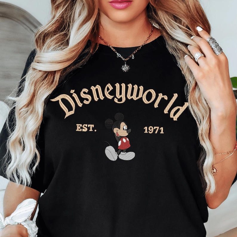A woman wearing a black t-shirt with the text "Disneyworld EST. 1971" and a Mickey Mouse graphic.