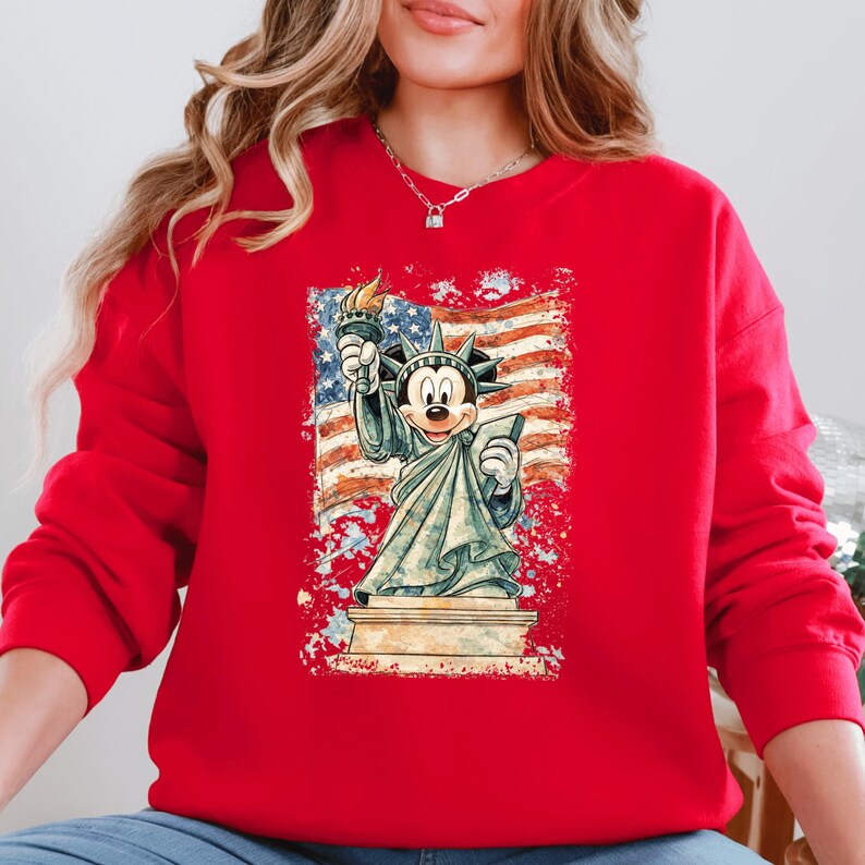 A woman wearing a red sweatshirt with a graphic of Mickey Mouse holding the torch of freedom in front of the Statue of Liberty.