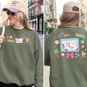 A woman wearing a green sweatshirt with a pig design and various colorful illustrations on the back.