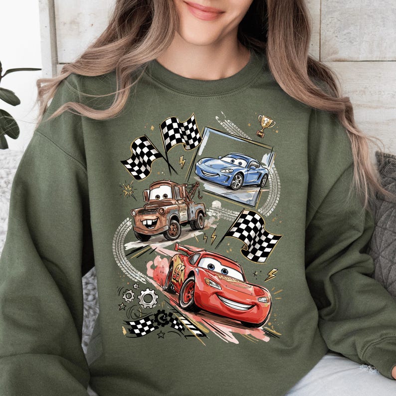 A woman wearing a green sweatshirt with a graphic design featuring cartoon cars and checkered flags.
