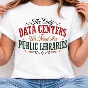 May include: A white short-sleeved t-shirt featuring the text The Only DATA CENTERS We Need Are PUBLIC LIBRARIES in a mix of green, red, and orange colors with decorative stars and flourishes printed on the front of the garment.