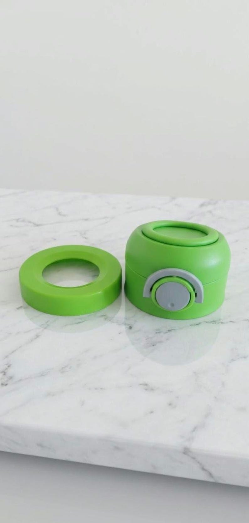 Puede incluir: Un juego de tapa y base de botella de agua de color verde brillante. La tapa es un anillo circular, y la base es un cilindro redondeado con un bot&oacute;n gris. El juego es de pl&aacute;stico.