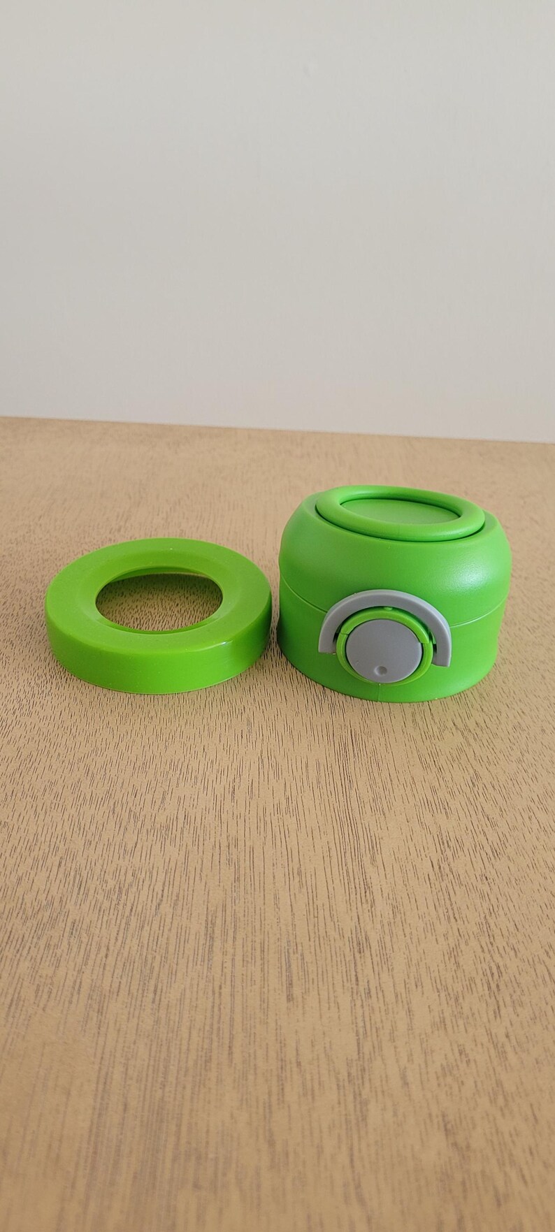 Puede incluir: Juego de tapa y tap&oacute;n verde para botella de agua. La tapa es una pieza plana y circular, y el tap&oacute;n es un cilindro redondeado con una palanca gris y blanca. El juego es de pl&aacute;stico.