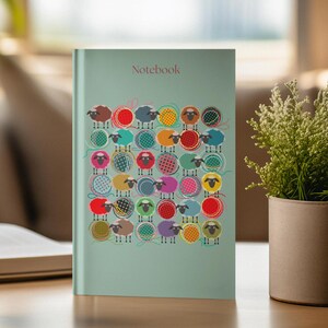 May include: A teal notebook with the word "Notebook" printed on the front cover. The cover features a colorful pattern of sheep standing on balls of yarn.