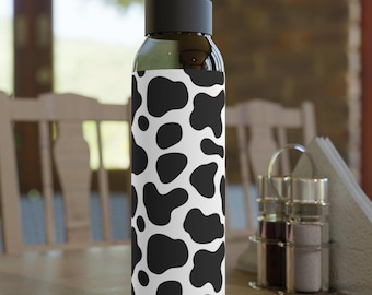 Può includere: Una bottiglia d'acqua in vetro trasparente con un motivo a mucca bianco e nero. La bottiglia ha un tappo nero e un manico per il trasporto.
