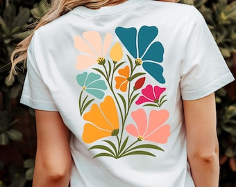 May include: White t-shirt featuring a colorful floral design on the back. The design includes flowers in shades of orange, pink, teal, and blue, with green stems and leaves. The shirt is made of a soft, comfortable material.
