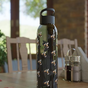 May include: A black reusable water bottle with a black lid and a carrying handle. The bottle has a pattern of bumblebees on it.