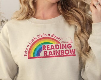 May include: A beige sweatshirt with a rainbow and the text "Take a Look, it's in a Book! Reading Rainbow" printed on the front.