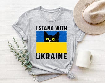 May include: A gray t-shirt with the text "I Stand With Ukraine" and a black cat peeking over the Ukrainian flag.