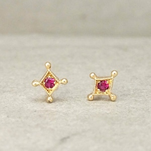 Peut inclure: Une paire de boucles d'oreilles en or avec une petite pierre rouge au centre de chaque boucle d'oreille. Les boucles d'oreilles ont la forme d'un carré aux coins arrondis.