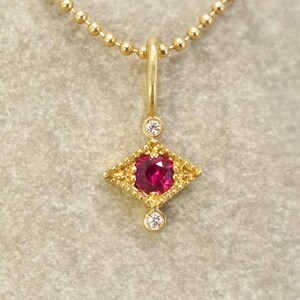 May include: A gold necklace with a pendant featuring a red gemstone surrounded by smaller diamonds in a geometric shape.