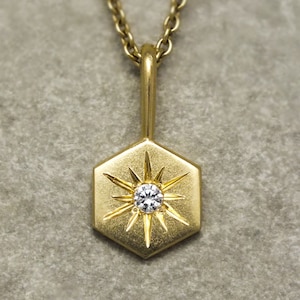 May include: A gold necklace with a hexagonal pendant featuring a starburst design with a small diamond in the center.