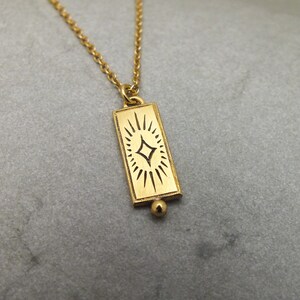 Może przedstawiać: Złoty naszyjnik z prostokątnym wisiorem przedstawiającym stylizowany wz&oacute;r gwiazdy.