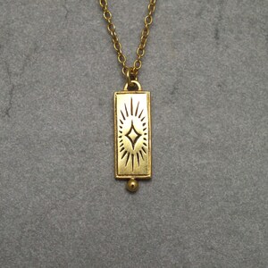 Może przedstawiać: Złoty naszyjnik z prostokątnym wisiorem przedstawiającym stylizowany wz&oacute;r gwiazdy.