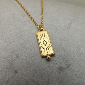 Może przedstawiać: Złoty naszyjnik z łańcuszkiem i prostokątnym wisiorem z ozdobnym wzorem gwiazdy.