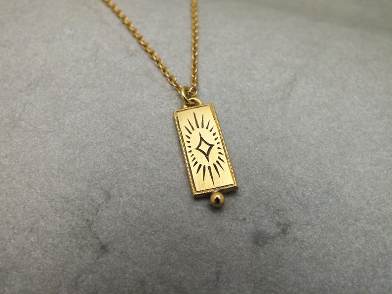 Może przedstawiać: Złoty naszyjnik z łańcuszkiem i prostokątnym wisiorem z ozdobnym wzorem gwiazdy.