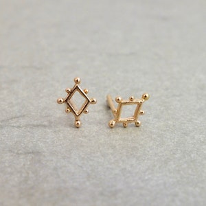 May include: A pair of gold earrings with a geometric design. The earrings are in the shape of a diamond and a square.