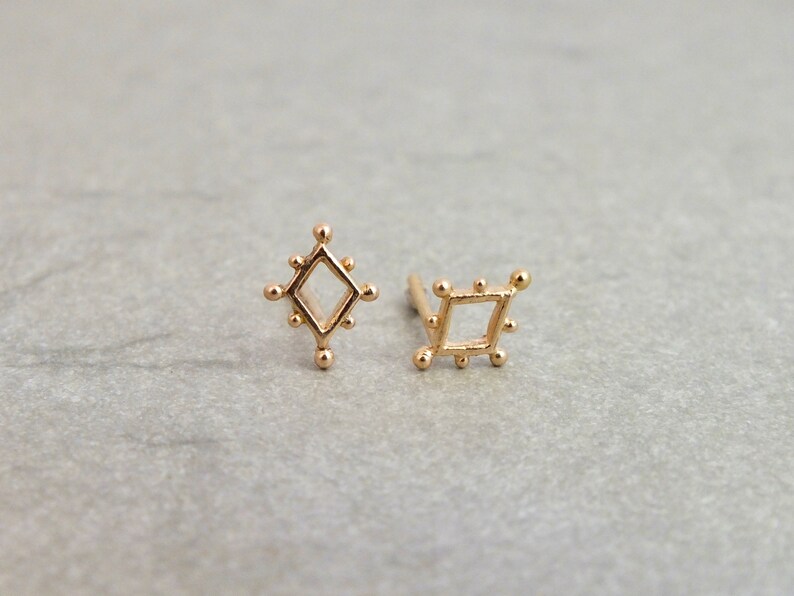 May include: A pair of gold earrings with a geometric design. The earrings are in the shape of a diamond and a square.