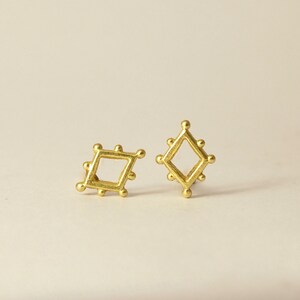 May include: A pair of gold-toned earrings with a geometric design. Each earring features a square shape with a smaller square cut out in the center.