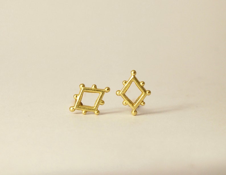 May include: A pair of gold-toned earrings with a geometric design. Each earring features a square shape with a smaller square cut out in the center.