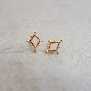 May include: A pair of gold diamond-shaped earrings with a textured surface.