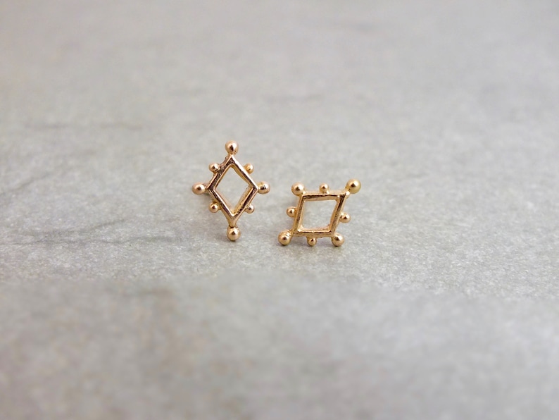 May include: A pair of gold diamond-shaped earrings with a textured surface.