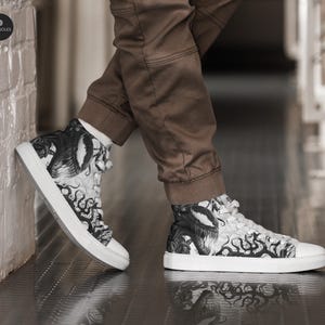 Pu&ograve; includere: Sneakers bianche in tela alte con una stampa grafica in bianco e nero di una creatura con tentacoli. La stampa sembra essere un'illustrazione stilizzata di un mostro.