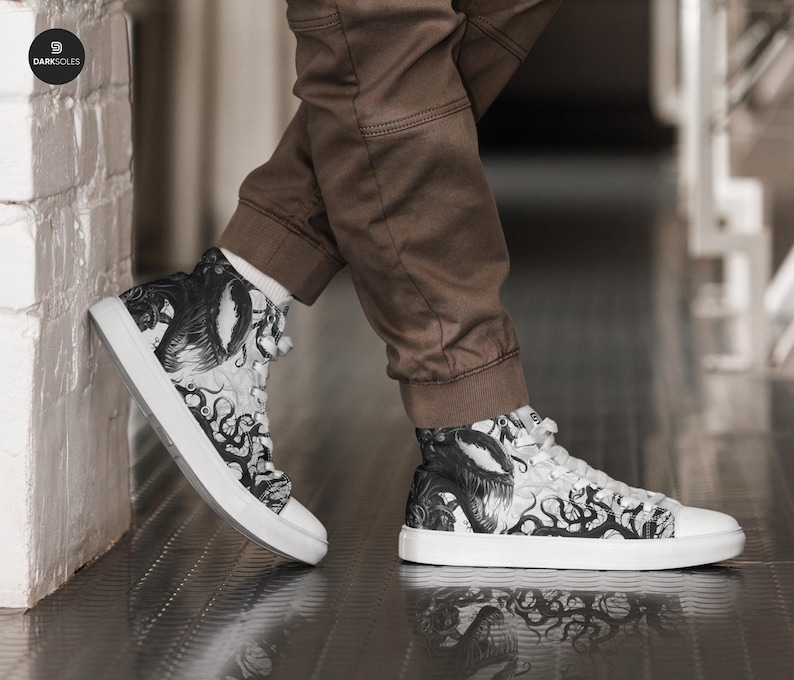 Pu&ograve; includere: Sneakers bianche in tela alte con una stampa grafica in bianco e nero di una creatura con tentacoli. La stampa sembra essere un'illustrazione stilizzata di un mostro.