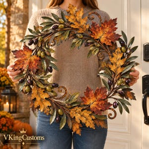 Può includere: Una ghirlanda decorativa circolare con foglie di quercia in metallo nei toni dell'arancione, giallo e marrone, intervallate da accenti a forma di oliva di colore verde e viola scuro. Il design include rami in metallo a spirale.